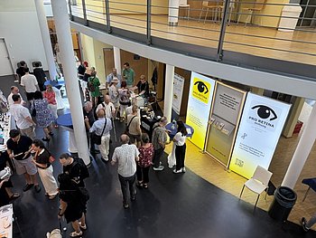 Blick von oben auf das Foyer. Hier sieht man den Messestand der PRO RETINA. Viele Menschen sind hier versammelt.